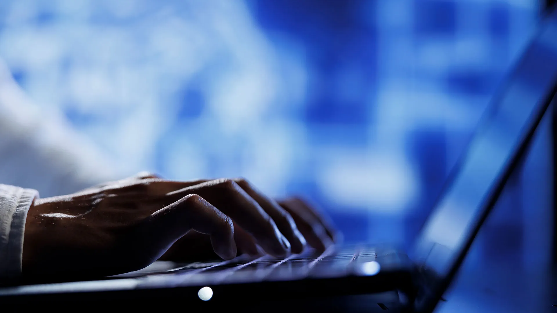 Close-up of hands typing on a laptop keyboard against a blue digital backdrop